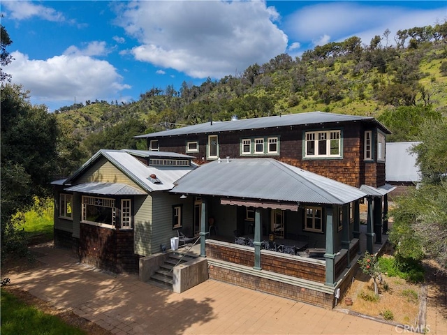 view of front of home featuring covered porch, a wooded view, metal roof, and a patio