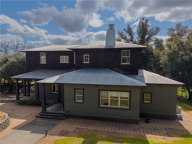 rear view of house featuring a patio, a chimney, and metal roof