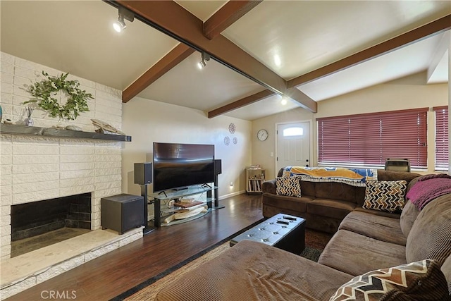 living area featuring wood finished floors, rail lighting, a fireplace, baseboards, and vaulted ceiling with beams