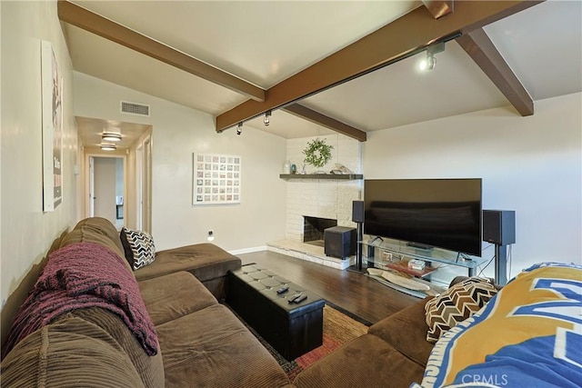 living area featuring visible vents, wood finished floors, rail lighting, a fireplace, and vaulted ceiling with beams