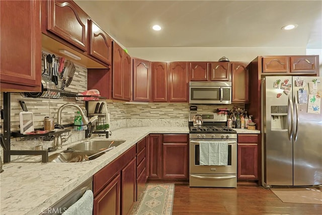 kitchen featuring dark wood finished floors, light stone counters, decorative backsplash, appliances with stainless steel finishes, and a sink