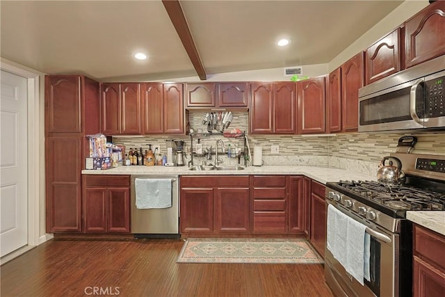 kitchen with tasteful backsplash, dark wood finished floors, beamed ceiling, appliances with stainless steel finishes, and a sink