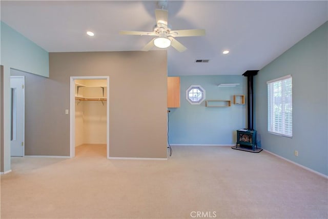 unfurnished living room with a wood stove, plenty of natural light, visible vents, and ceiling fan