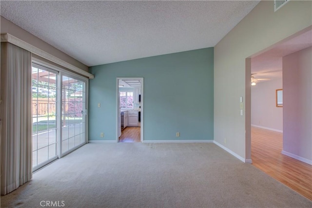 empty room with light carpet, a textured ceiling, baseboards, and lofted ceiling