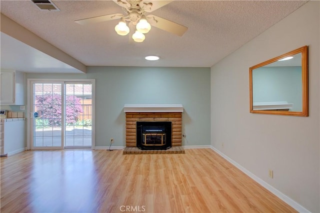 unfurnished living room featuring visible vents, light wood-style flooring, ceiling fan, a textured ceiling, and a brick fireplace