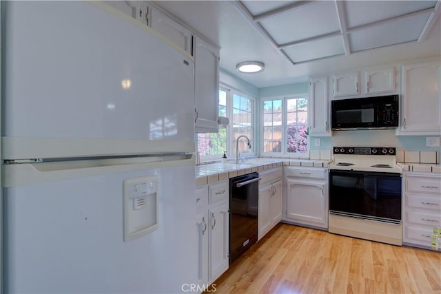 kitchen featuring light wood finished floors, white cabinets, black appliances, and a sink