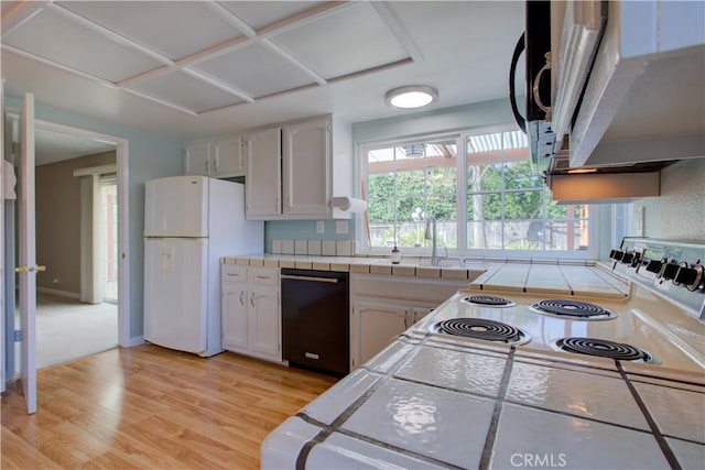 kitchen featuring tile counters, dishwasher, light wood-style flooring, freestanding refrigerator, and a sink