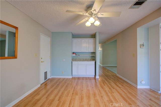 kitchen featuring light wood finished floors, visible vents, white cabinetry, ceiling fan, and a textured ceiling