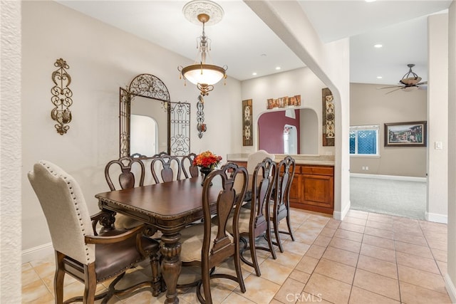 dining area with light tile patterned floors, baseboards, arched walkways, and ceiling fan