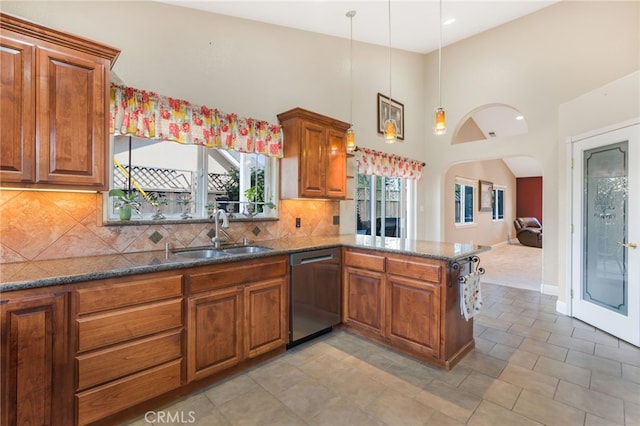 kitchen featuring tasteful backsplash, dishwasher, dark stone counters, brown cabinetry, and a sink