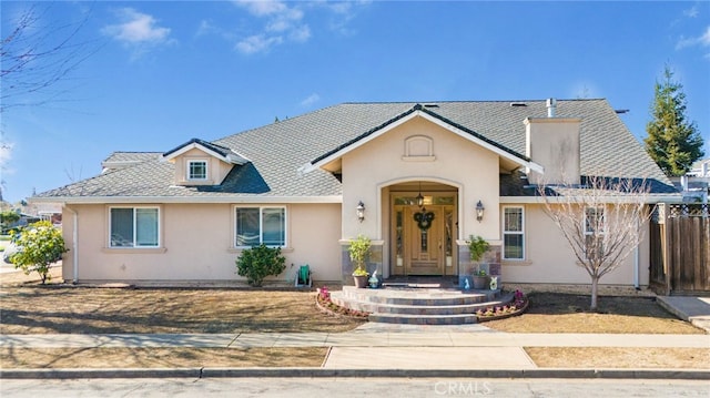 view of front facade featuring stucco siding, a shingled roof, and fence