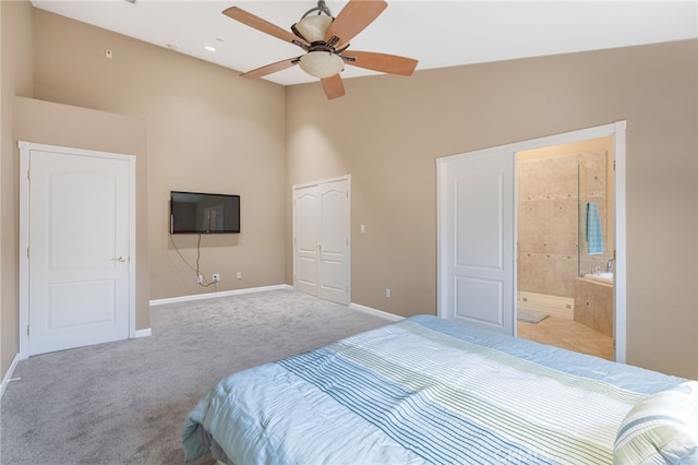 carpeted bedroom with a ceiling fan, baseboards, ensuite bath, a high ceiling, and a closet