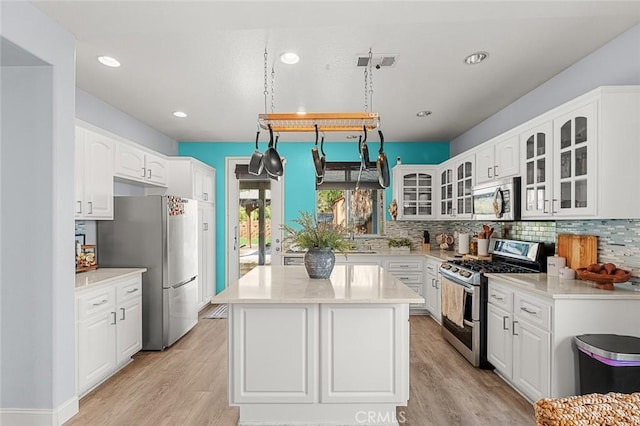 kitchen with visible vents, light wood-style flooring, backsplash, appliances with stainless steel finishes, and glass insert cabinets