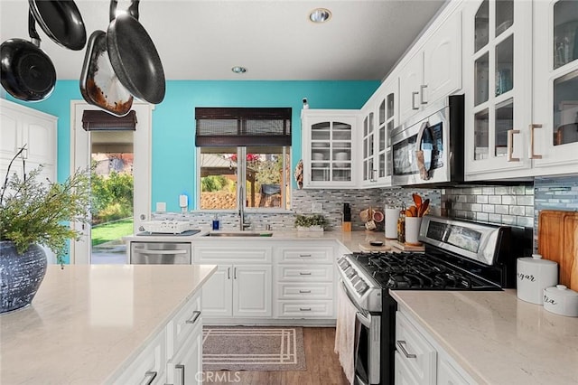 kitchen with backsplash, light stone countertops, appliances with stainless steel finishes, white cabinets, and a sink