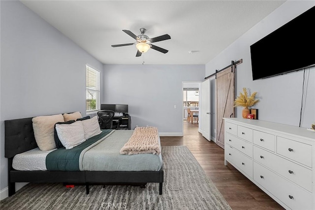 bedroom with baseboards, dark wood-type flooring, a barn door, and a ceiling fan