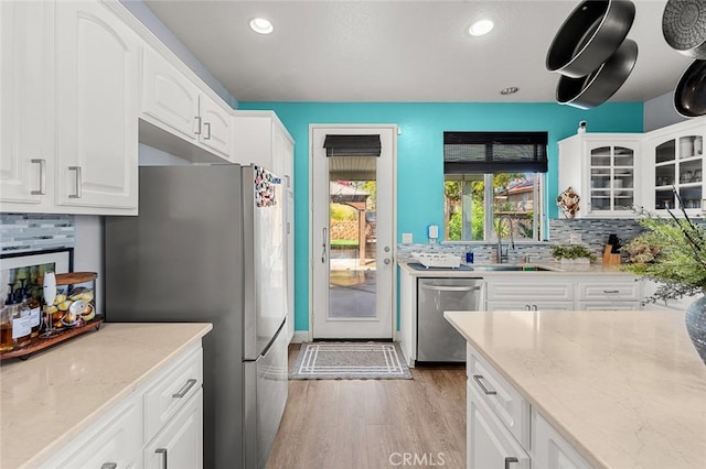 kitchen with a sink, stainless steel appliances, light wood-style floors, glass insert cabinets, and light stone countertops