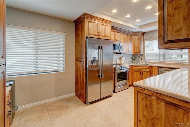 kitchen featuring baseboards, light tile patterned flooring, a sink, decorative backsplash, and stainless steel appliances