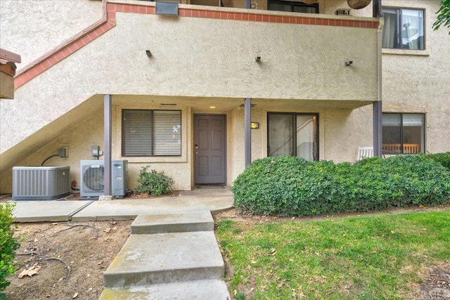 property entrance with stucco siding, central AC unit, and ac unit