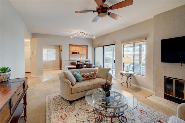 living area with baseboards, ceiling fan, a tiled fireplace, rail lighting, and light tile patterned flooring