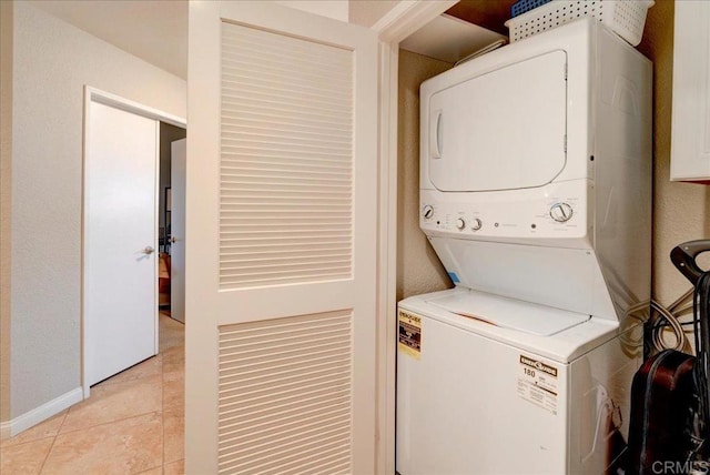 washroom with laundry area, stacked washer / dryer, light tile patterned floors, and baseboards