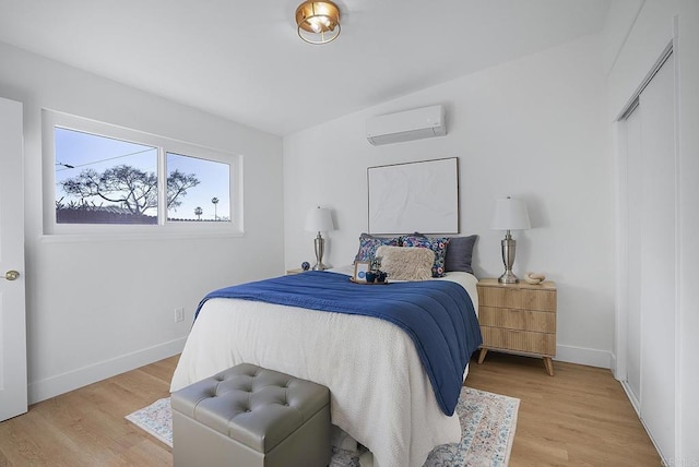 bedroom featuring baseboards, an AC wall unit, and light wood-style floors