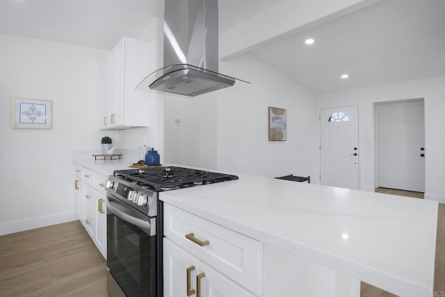 kitchen featuring wall chimney range hood, light wood-type flooring, light stone counters, stainless steel gas stove, and white cabinets