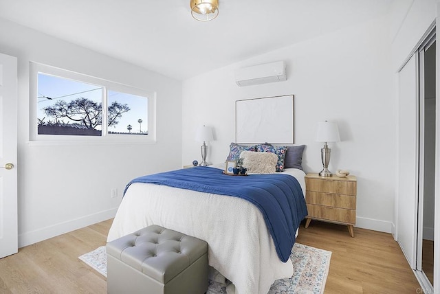 bedroom with a wall mounted air conditioner, baseboards, and light wood finished floors