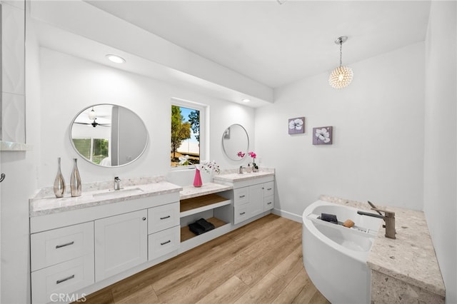 full bath featuring a freestanding bath, two vanities, wood finished floors, and a sink