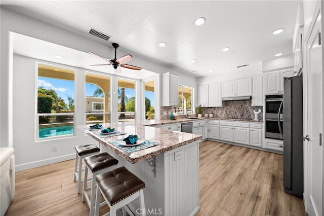 kitchen with light wood-style flooring, a kitchen breakfast bar, tasteful backsplash, appliances with stainless steel finishes, and white cabinets