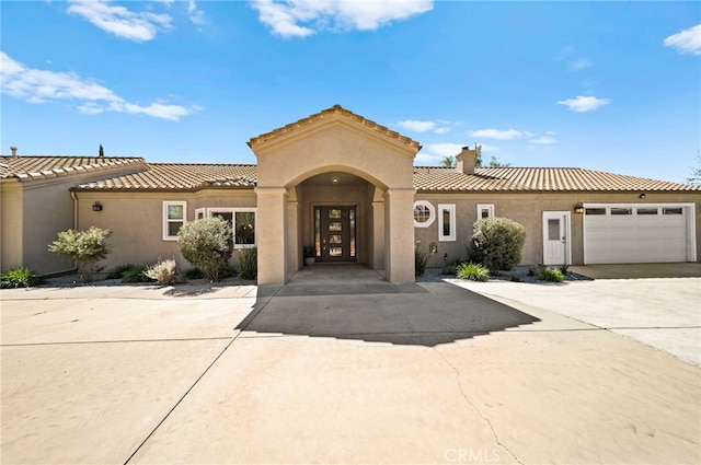 mediterranean / spanish-style house with an attached garage, a chimney, stucco siding, concrete driveway, and a tile roof