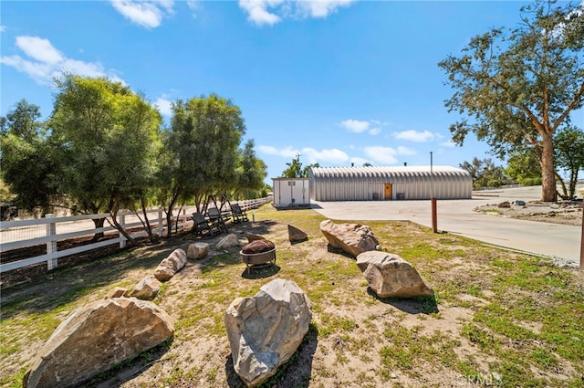 view of yard with an outbuilding, fence, a pole building, and an outdoor fire pit