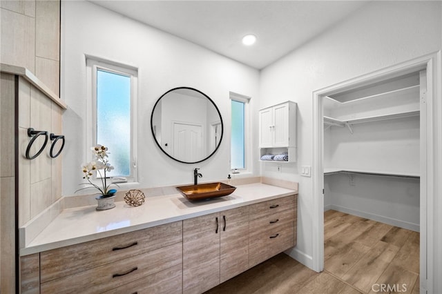 bathroom with a spacious closet, baseboards, recessed lighting, wood finished floors, and vanity