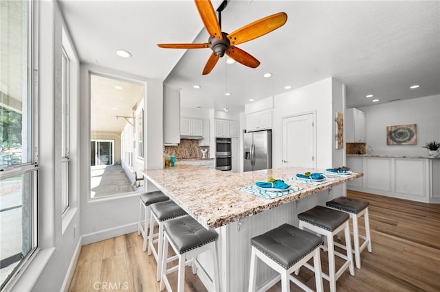 kitchen featuring tasteful backsplash, appliances with stainless steel finishes, white cabinetry, and light wood-type flooring