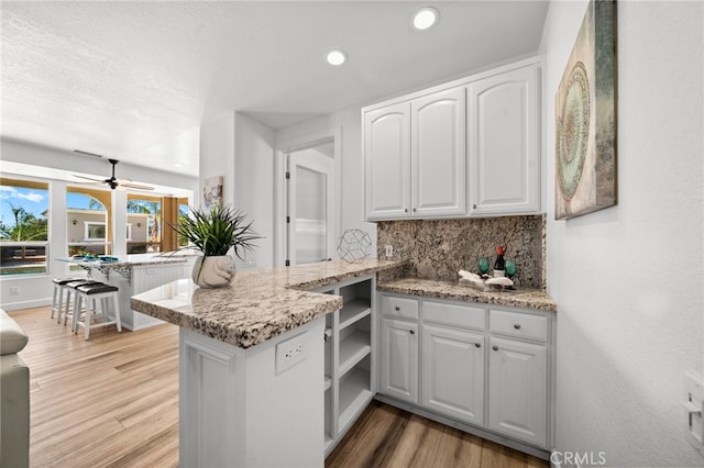 kitchen with light stone counters, backsplash, white cabinetry, a peninsula, and light wood finished floors