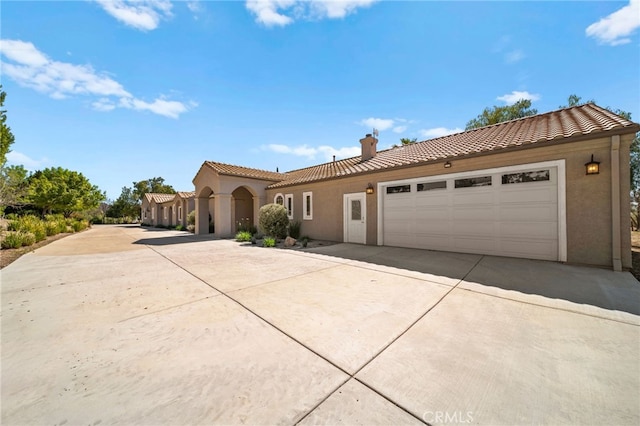 mediterranean / spanish-style home with stucco siding, a chimney, driveway, and a tiled roof