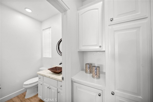 bathroom with toilet, vanity, baseboards, and wood finished floors