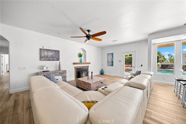 living area with arched walkways, a glass covered fireplace, light wood finished floors, and a ceiling fan