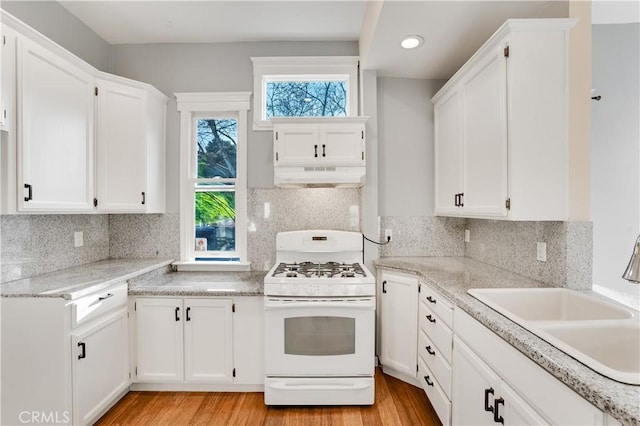 kitchen with under cabinet range hood, white range with gas stovetop, light wood-style flooring, white cabinets, and a sink