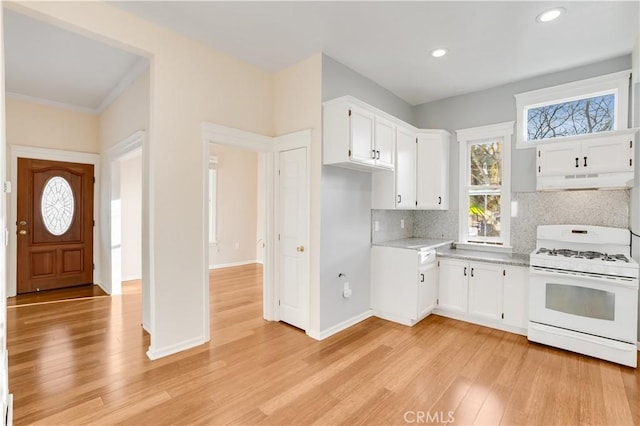 kitchen with light wood-type flooring, white range with gas cooktop, under cabinet range hood, backsplash, and white cabinets