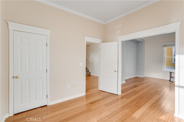 spare room featuring crown molding, stairway, baseboards, and light wood finished floors