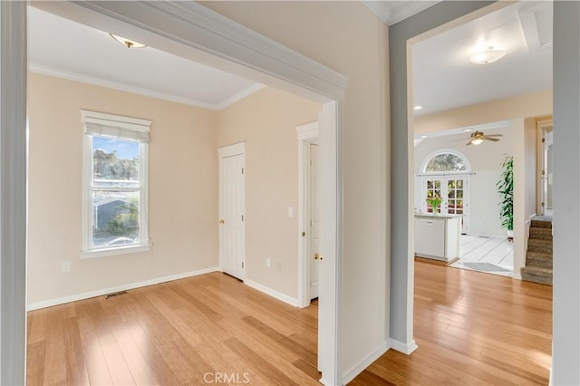 interior space featuring light wood-type flooring, baseboards, ceiling fan, and crown molding