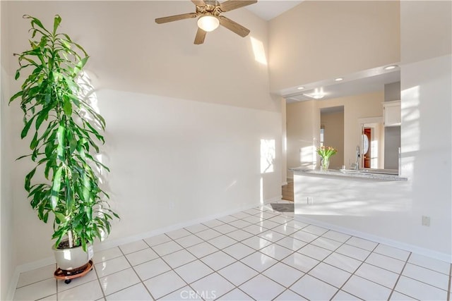 unfurnished living room with a ceiling fan, plenty of natural light, light tile patterned flooring, baseboards, and a towering ceiling