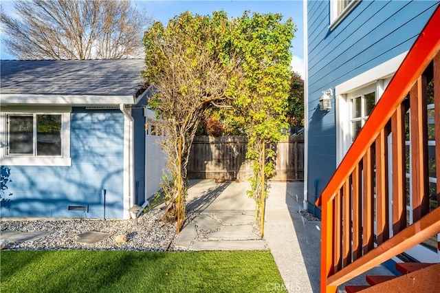 view of side of property with a patio area, fence, crawl space, and a shingled roof