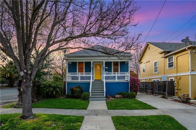 view of front of house with covered porch, stairs, a yard, and fence