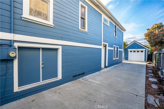 view of side of home with an outbuilding, driveway, a detached garage, fence, and a patio area