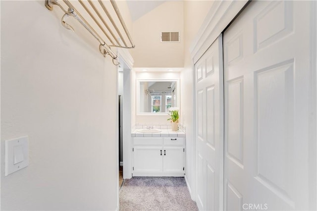 corridor with a sink, visible vents, light carpet, and lofted ceiling