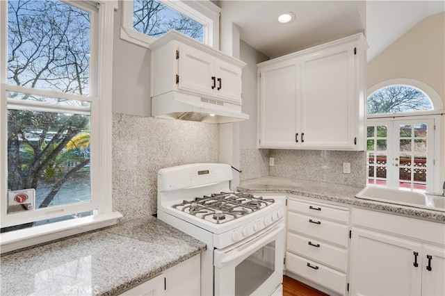 kitchen featuring light stone countertops, decorative backsplash, under cabinet range hood, white cabinetry, and white gas range