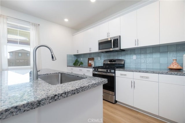 kitchen with light wood-type flooring, a sink, light stone counters, appliances with stainless steel finishes, and decorative backsplash