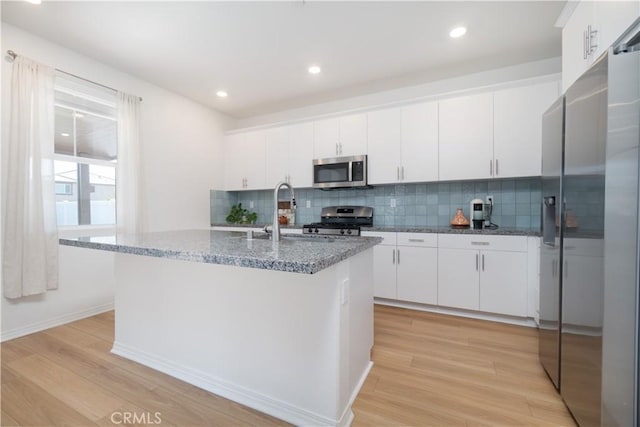 kitchen featuring light wood finished floors, stone countertops, appliances with stainless steel finishes, and a sink