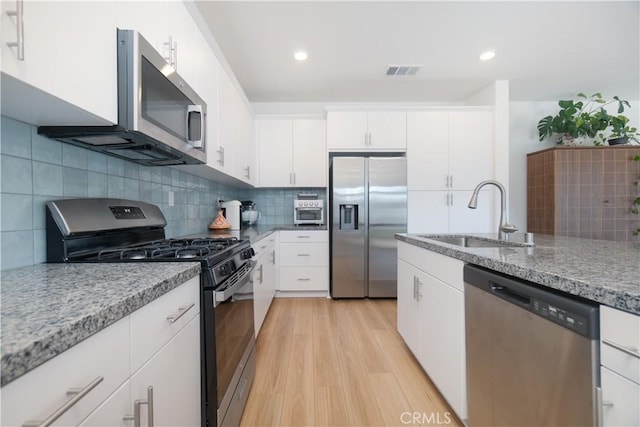 kitchen featuring visible vents, light wood-style flooring, a sink, appliances with stainless steel finishes, and tasteful backsplash